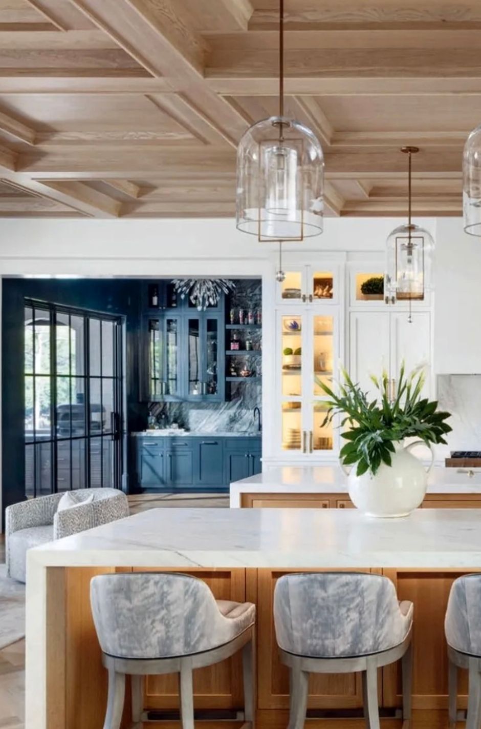 A kitchen beneath a white oak coffered ceiling, opening to a panelled blue bar