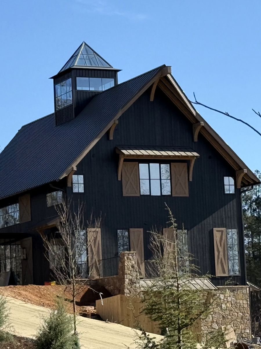 A black board-and-batten barn with heavy timber brackets and a glazed cupola